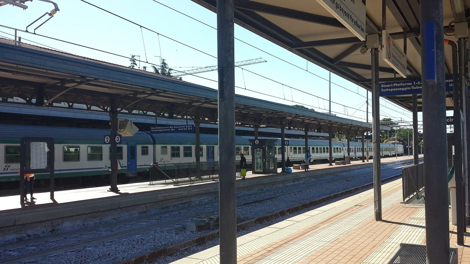 Binari e pensiline della stazione ferroviaria di Cecina con un treno regionale fermo al marciapiede in una giornata di sole