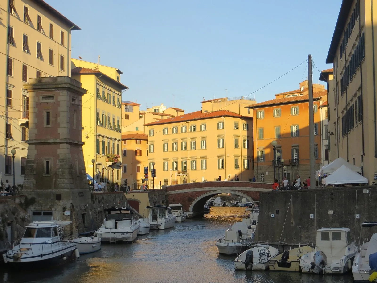 Scali del Ponte di Marmo nella Venezia Nuova di Livorno: canale con barche ormeggiate, ponte in mattoni e palazzi color ocra nella luce del tramonto
